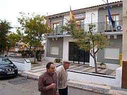 Dos vecinos pasan por delante del edificio del ayuntamiento con las banderas constitucionales./